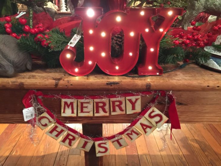 Christmas merchandise sold at Kaffie Frederick. In the photo is a light-up sign that says JOY (The color of the sign is red) and a garland banner that says Merry Christmas (The colors are cream and red)