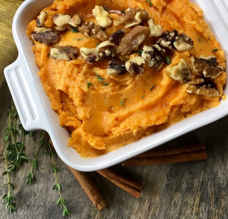 A photo of creamy mashed sweet potatoes in a casserole dish with pecans on top.