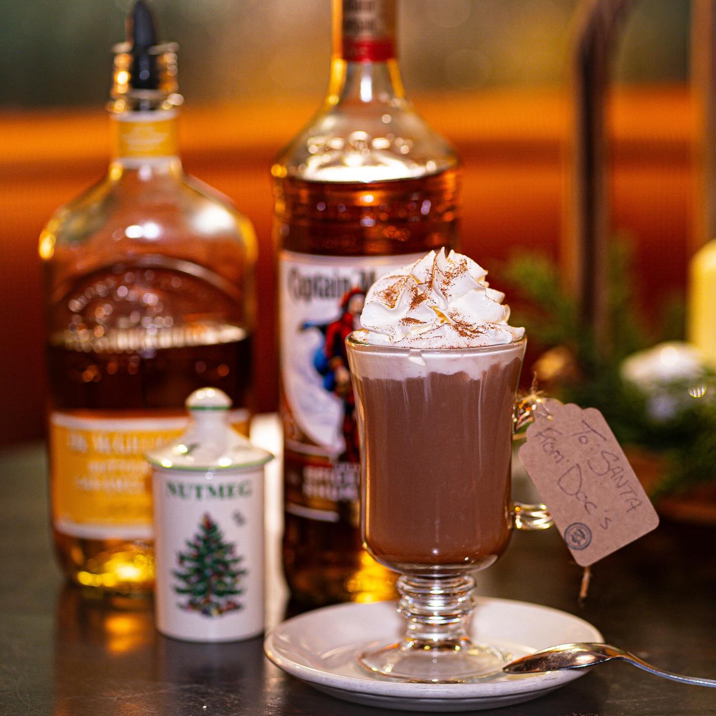 Photo of a cup of hot chocolate with a couple liquor bottles in the background.