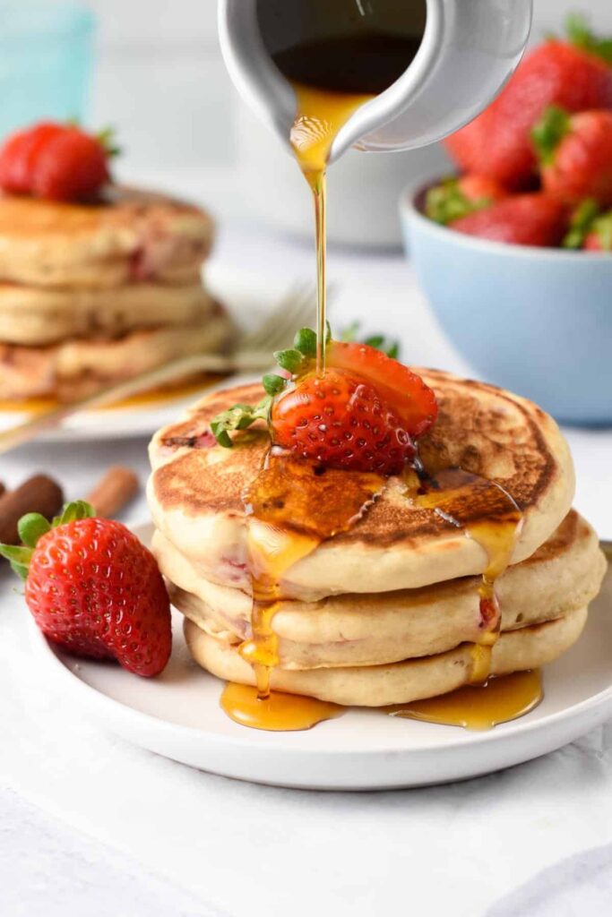 stack of pancakes topped with strawberries and syrup.