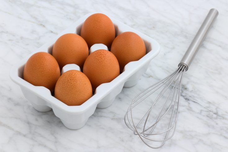 brown eggs in a white carton next to a metal whisk