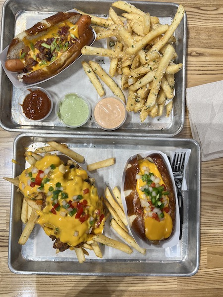 display of loaded dogs and fries on silver metal trays with white paper under the food