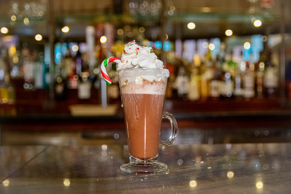 Photo of a cup hot chocolate with whipped cream and a candy cane.