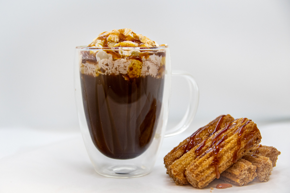 A photo of a cup of Hot Chocolate with mini churros next to the cup.