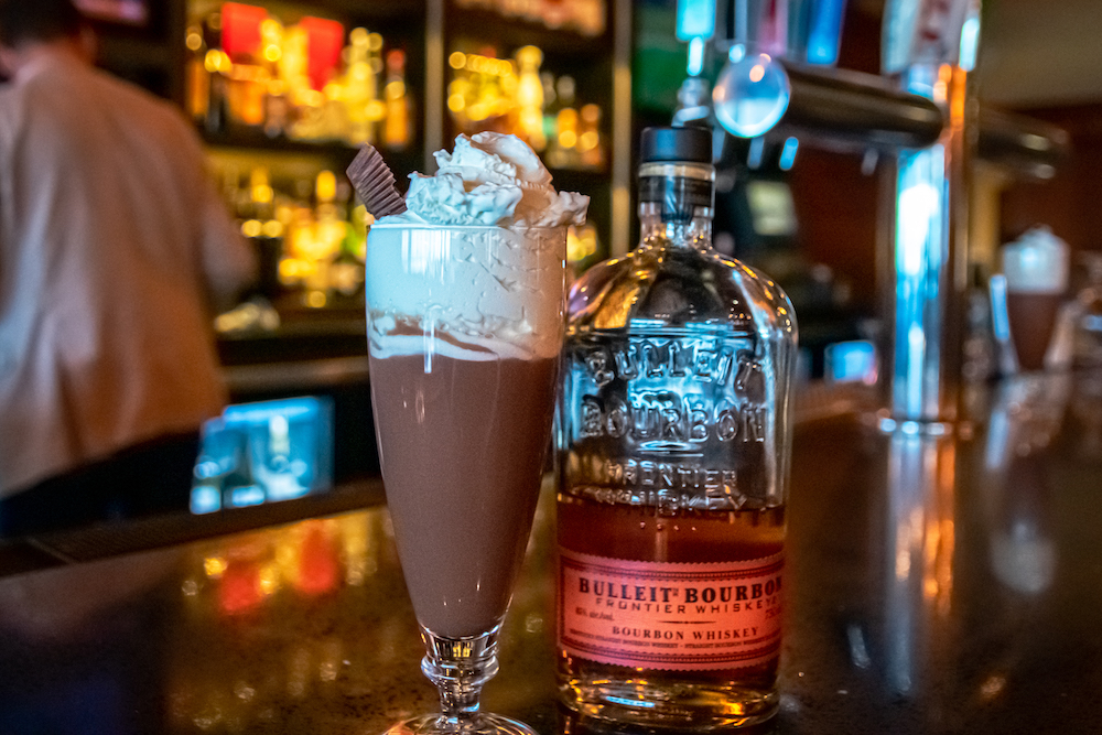photo of Hot Chocolate on a bar next to a bottle of Bulleit Bourbon.