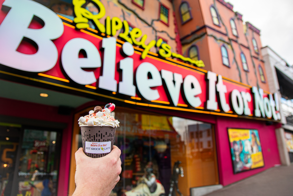 Photo of a hand holding a Hot Chocolate in front of Ripley's Believe It or Not building.