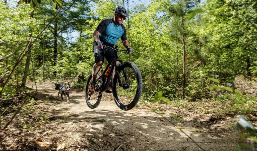 Mountain biker on a nature trail with dog running behind the bike.