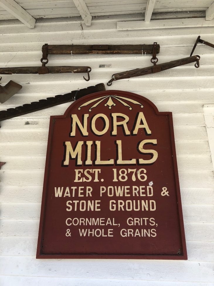 A photot of a sign saying Nora Mills EST 1876 Water Powered & Stone Ground. Cornmeal, Grits & Whole Grains.