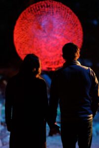 Rock City Flora Fluna red ball lantern with couple standing in front of it at night.