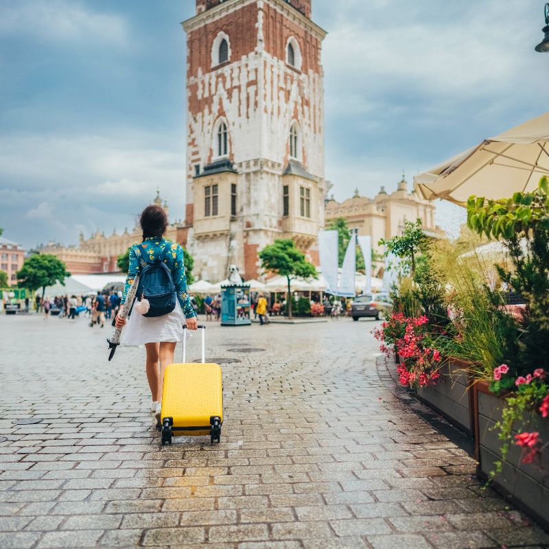 Student pulling a suitcase walking towards a building on a brick street.