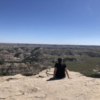girl sitting on rock, back to camera, looking out over the landscape of theodore roosevelt national park