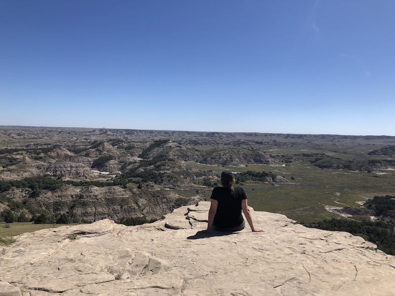 girl sitting on rock, back to camera, looking out over the landscape of theodore roosevelt national park