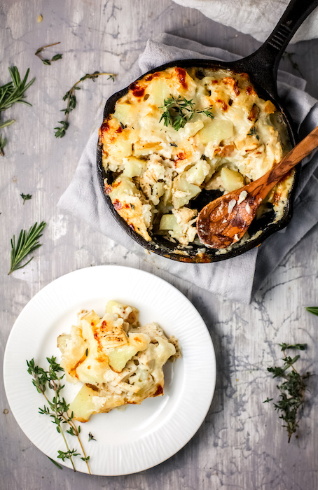 Photo of turkey potato casserole In a skillet with a slice taken out and is located on a plate next to the skillet. 