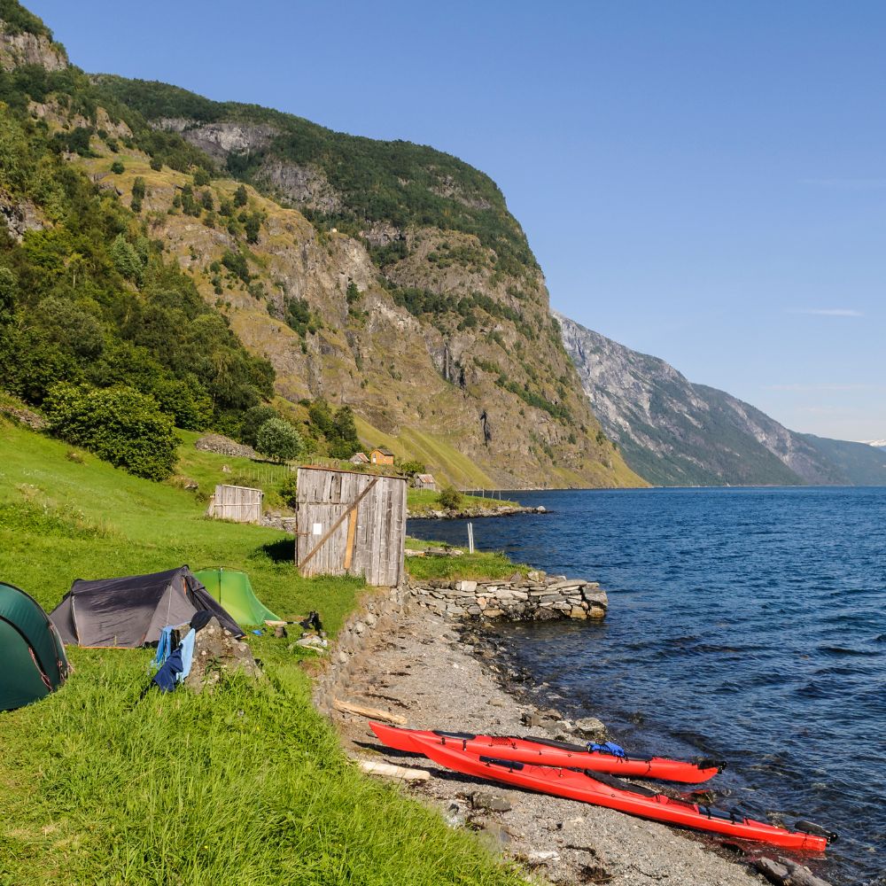 Kayaks on lake shore with tents nearby, best waterfront campsite.