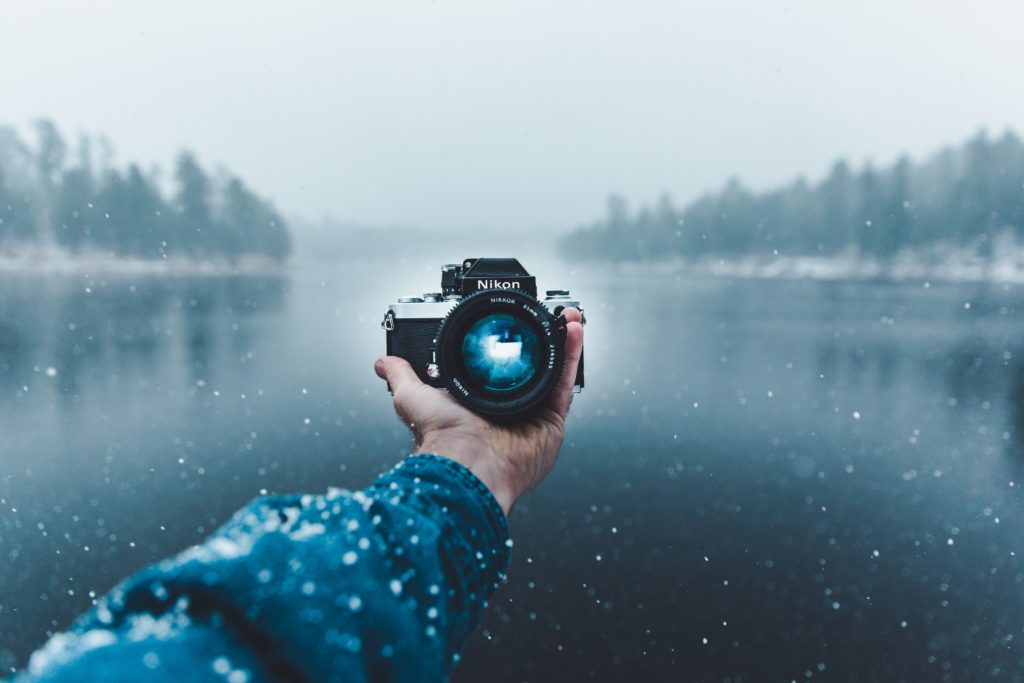 Hand holding a Nikon camera over water.