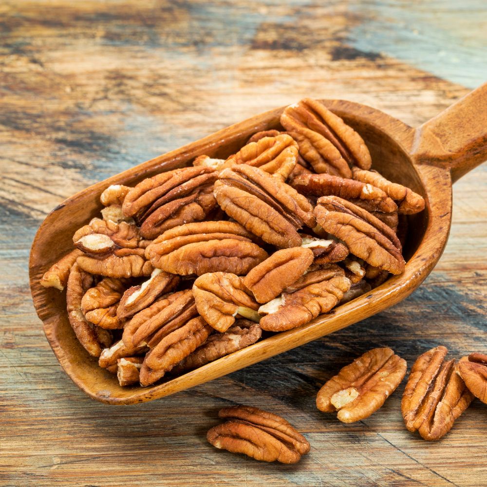 Wood scoop full of shelled, halved fresh pecans.