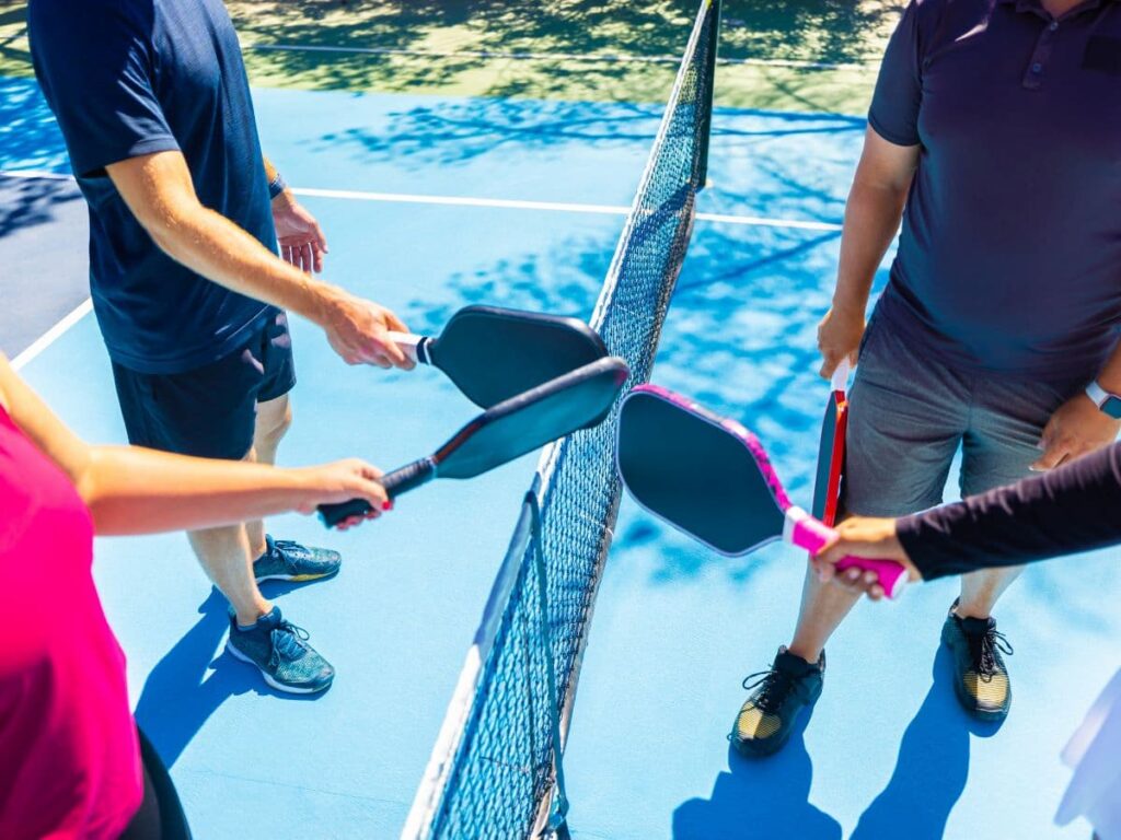 players holding pickleball  rackets next to the pickleball net.