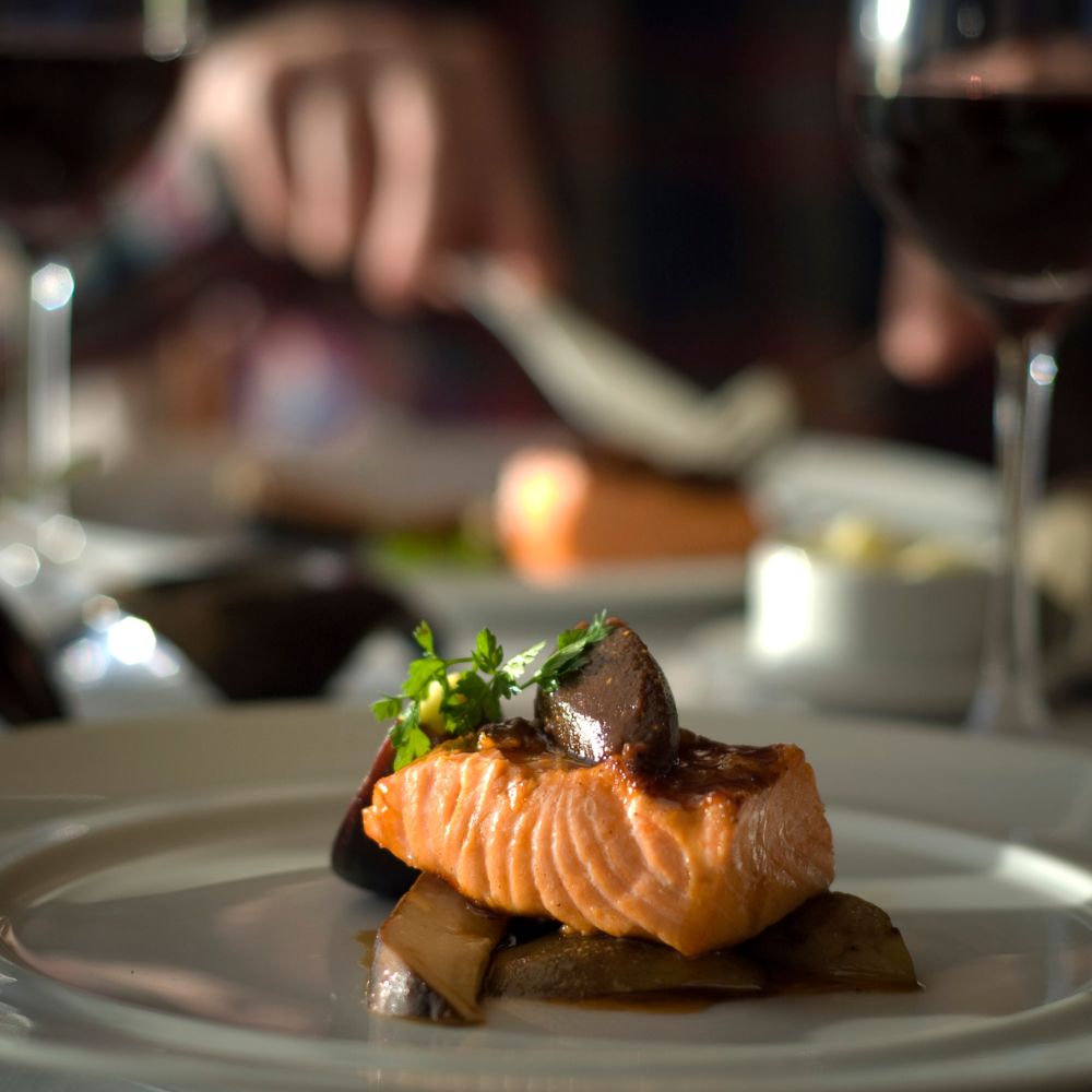 Cooked salmon topped with a few greens on a grey plate. 