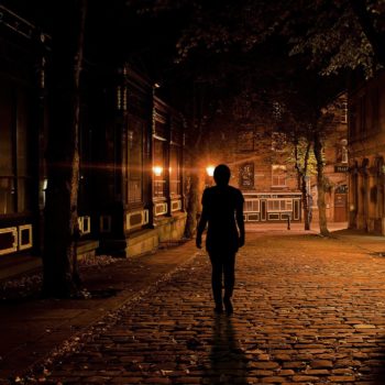 Lonely figure walking a desolate street at night with minimal light - wv ghost tours