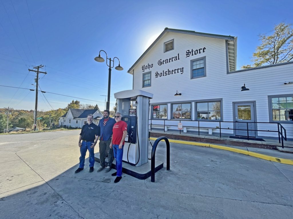 There men standing in front of a gas pump in the parking lot of Yoho General Store.